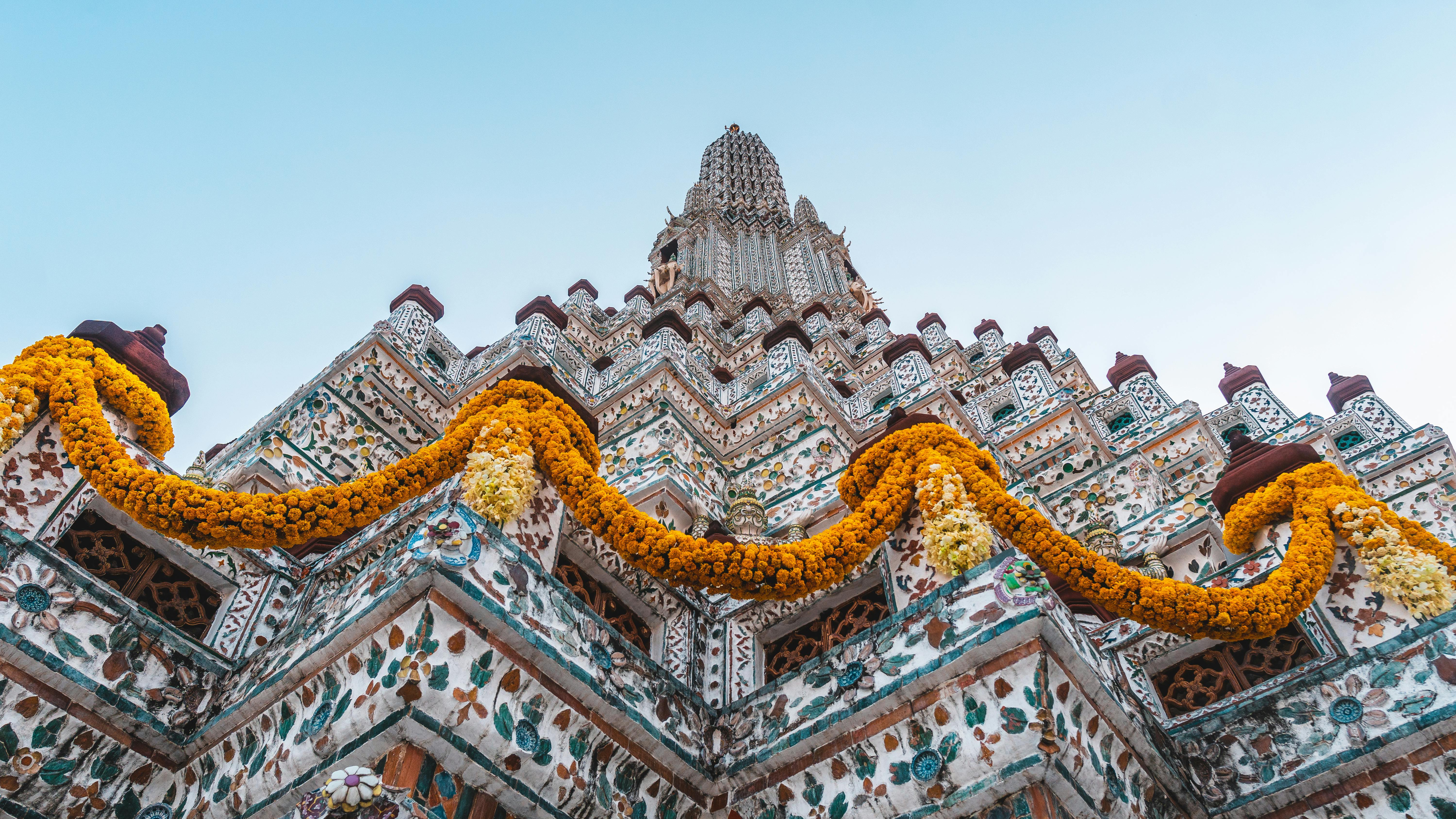Beautiful low angle view of Wat Arun temple adorned with yellow flowers in Bangkok, Thailand.