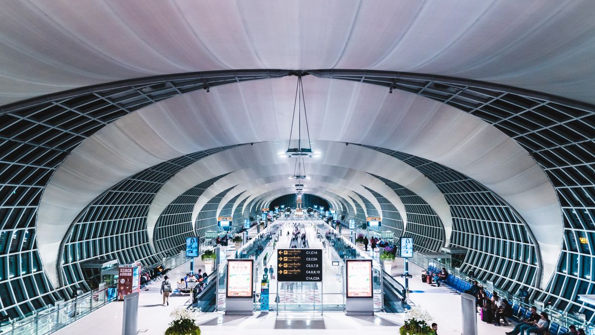 The sleek, modern check-in hall at Suvarnabhumi Airport, Bangkok, with travellers walking through.