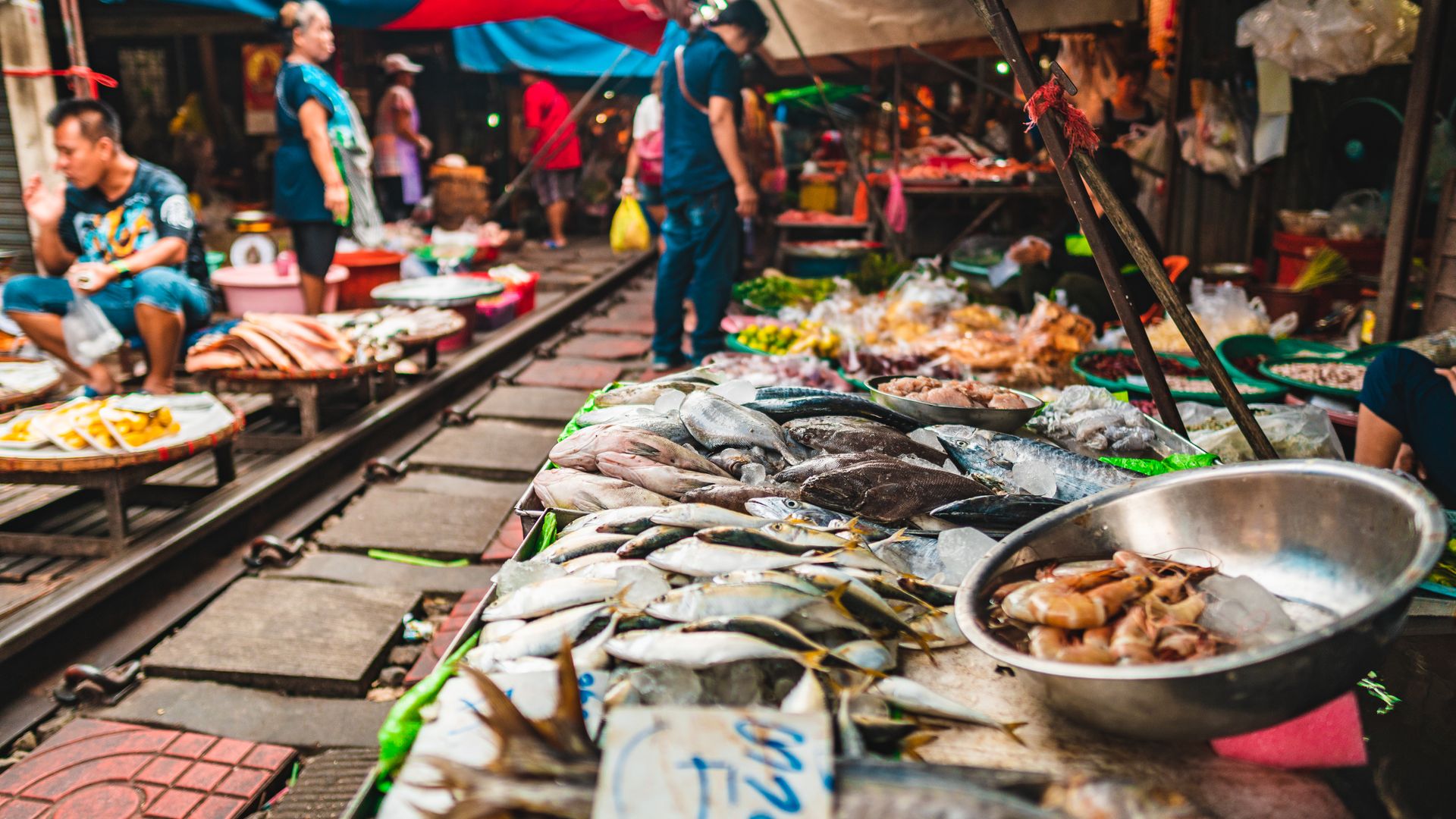 Bustling market scene along Bangkok railway featuring fresh seafood and local vendors.