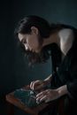 From above side view of young sad ethnic female leaning forward while touching broken mirror pieces in dark room