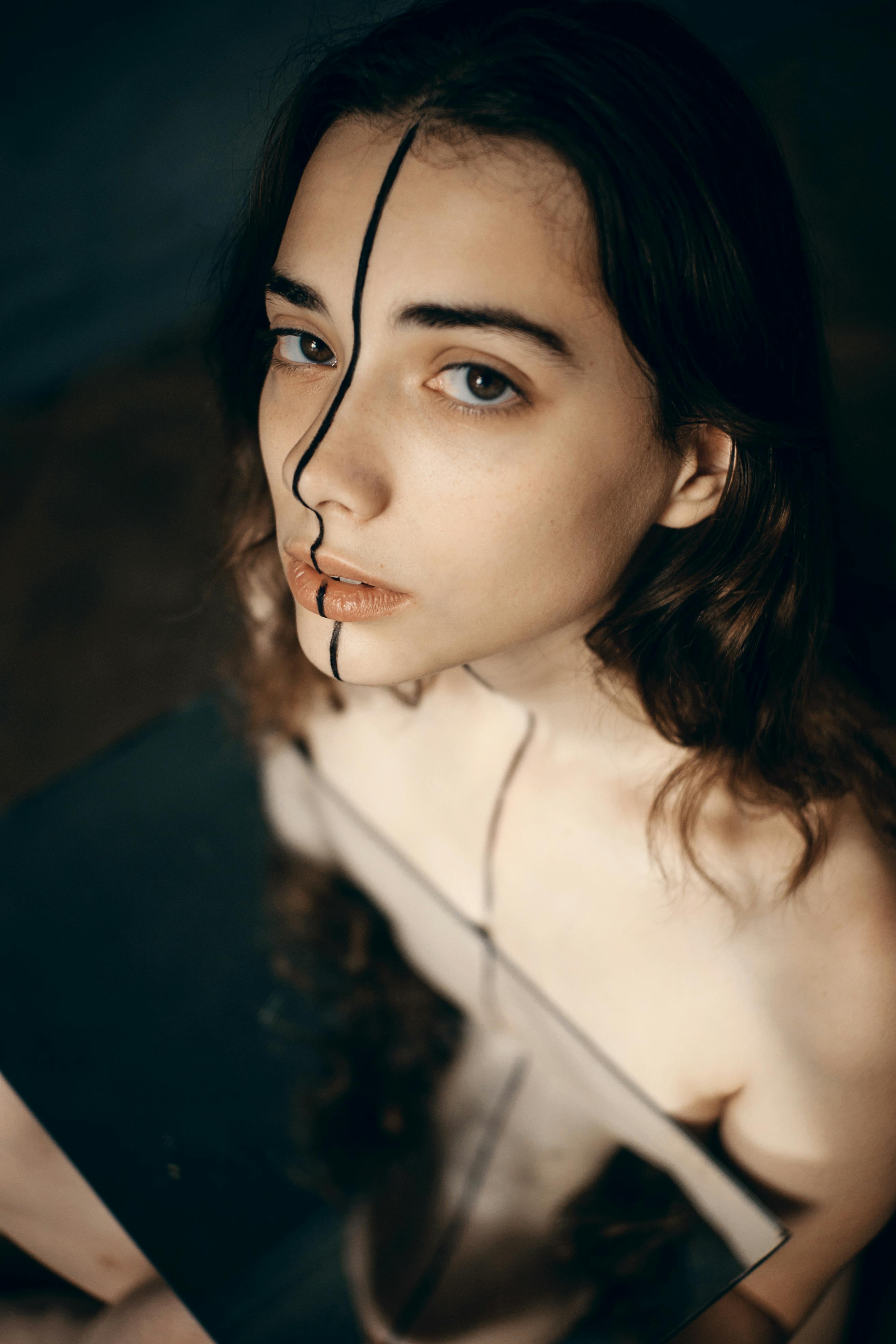 sad ethnic woman with greasepaint on face standing near mirror