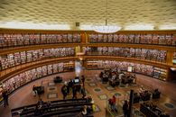 From above of contemporary city library interior with bookshelves illuminated by ceiling lamp with unrecognizable people walking on floor