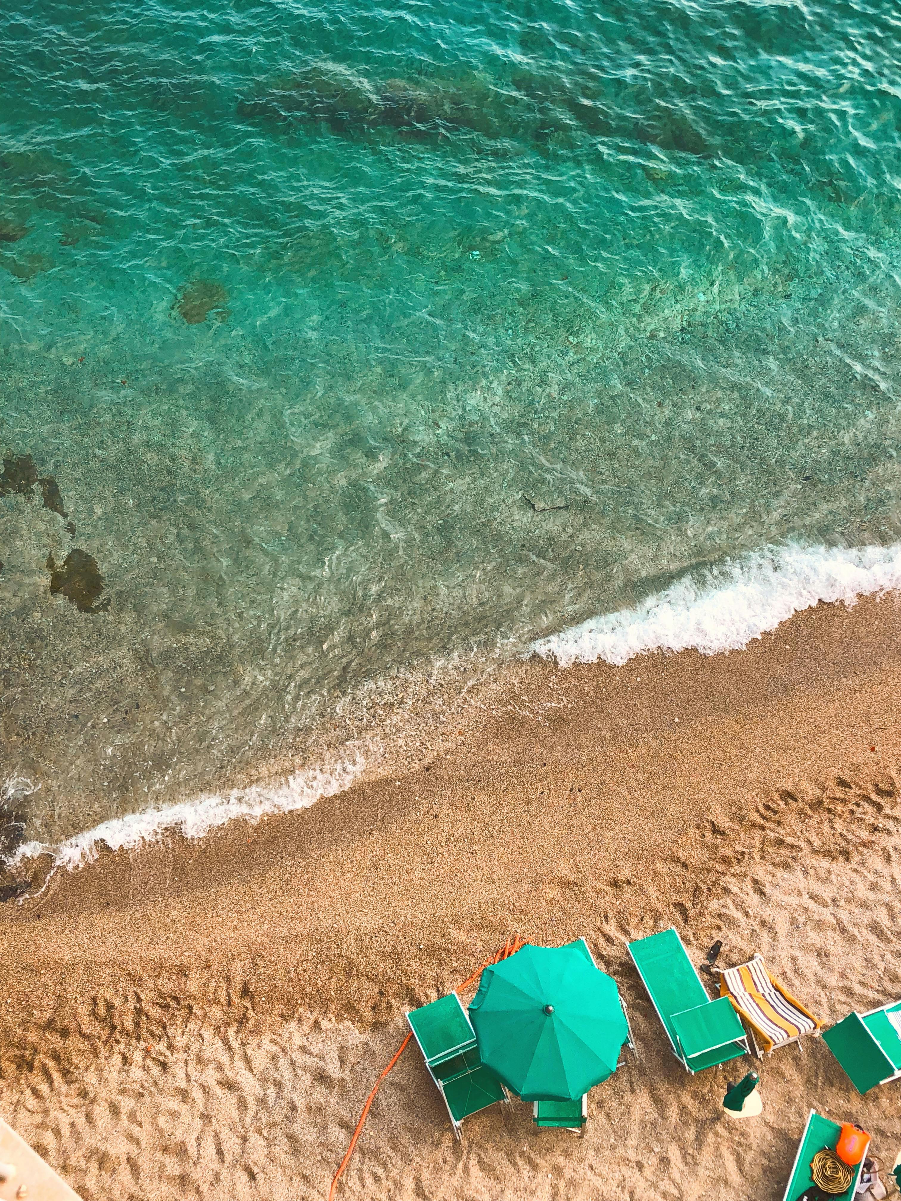 Green ocean near sandy beach with loungers and sun umbrella · Free