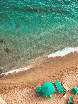 Drone view of bright wavy sea with transparent water near sandy shore with sun beds and umbrella in summer