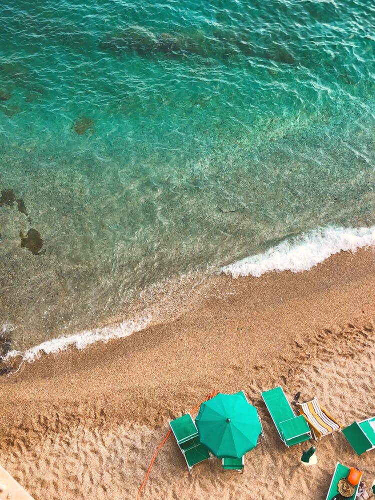 Green Ocean Near Sandy Beach With Loungers And Sun Umbrella