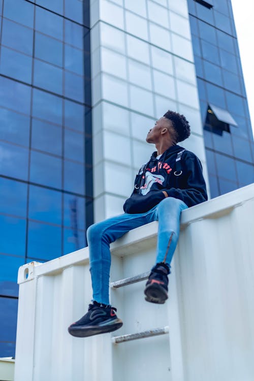 Unrecognizable trendy black man resting on fence near modern building