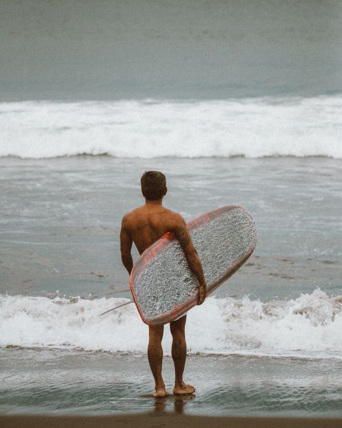 Free Man with surfboard standing by the ocean, ready to surf the waves. Stock Photo