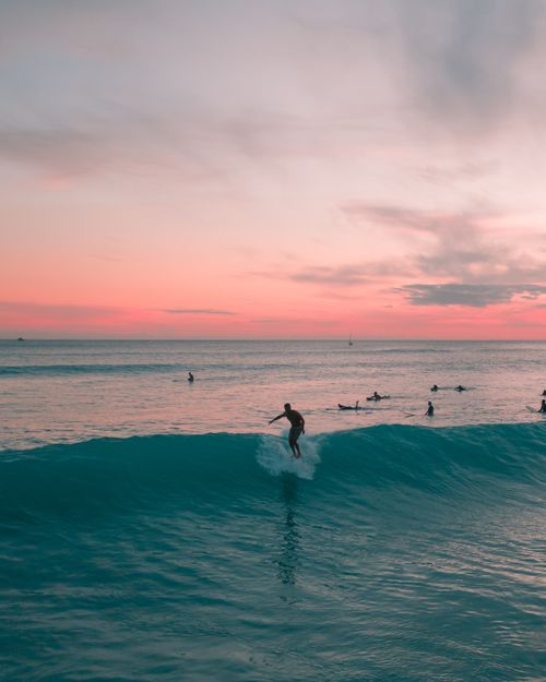 Free Surfer catching a wave at sunset in Hawaii with a vibrant sky. Stock Photo