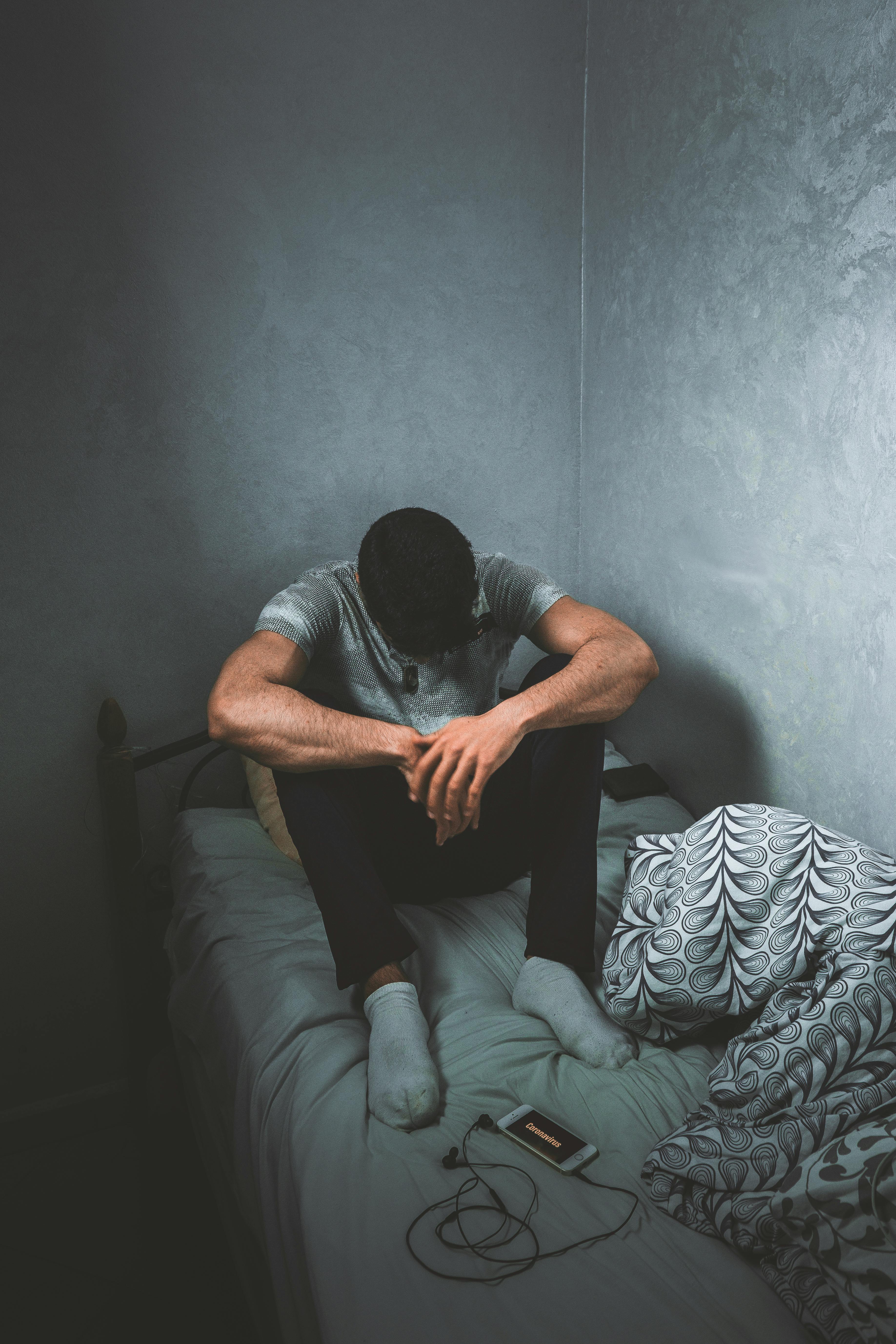 Free A man sits pensively on a bed in a dimly lit room, conveying emotion and introspection. Stock Photo