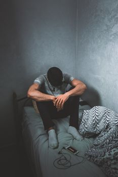 一名男子若有所思地坐在光线昏暗的房间里，坐在床上，流露出情感与内省