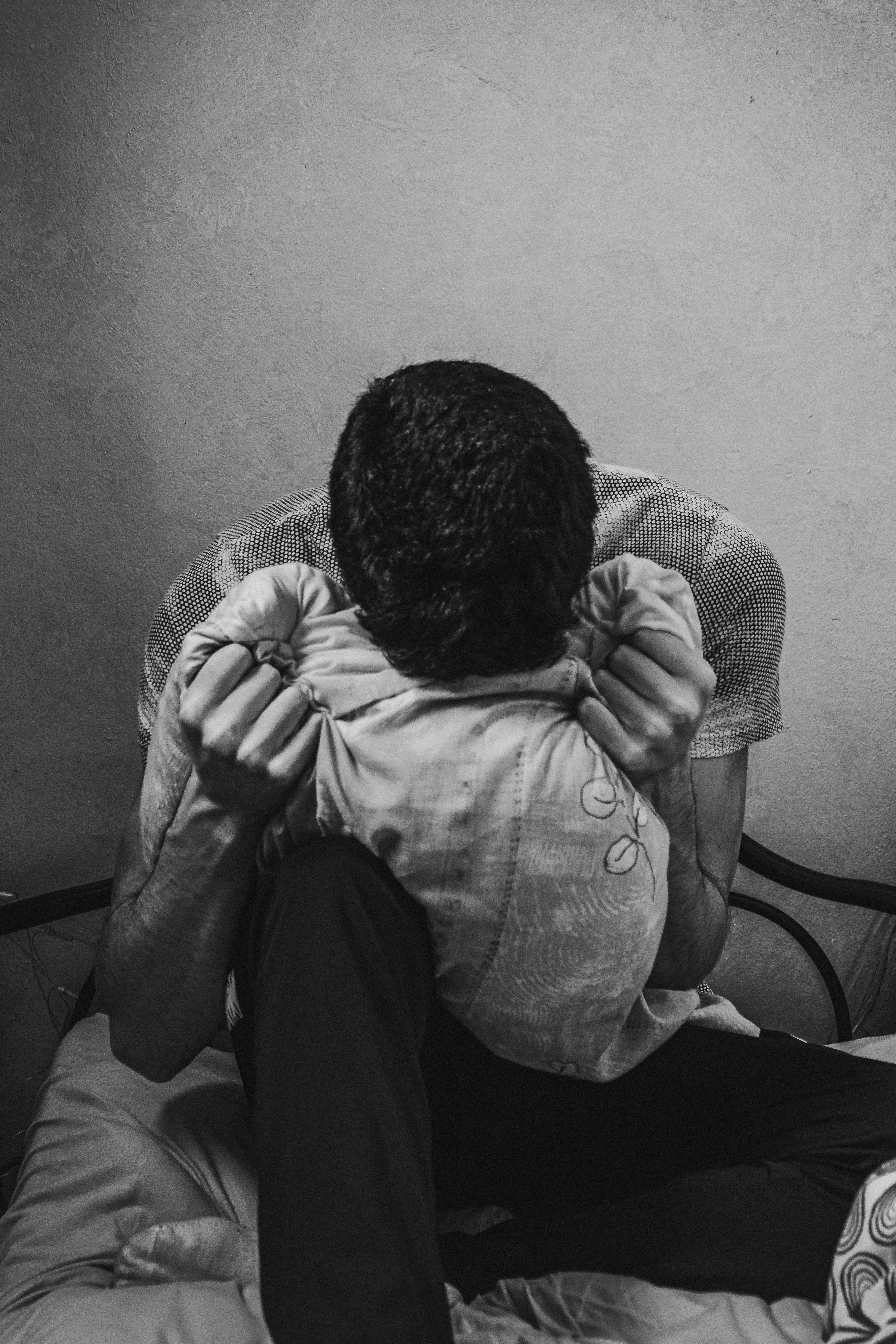 一张黑白图像中，一个沮丧的男人坐在床上，手拿枕头，表达着情感