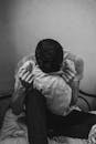 一张黑白图像中，一个沮丧的男人坐在床上，手拿枕头，表达着情感