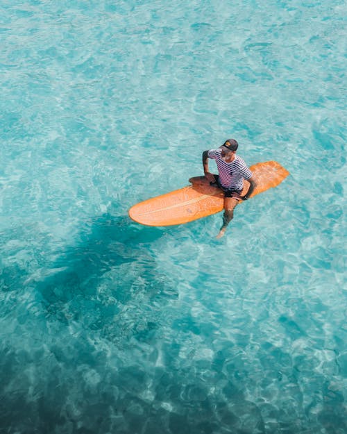Unrecognizable man sitting on surfboard on surface of water