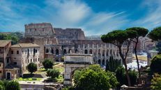 From above of aged masonry Colosseum and ancient arch near trees under bright blue cloudy sky in Italy