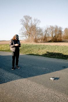 From above of anonymous male standing with remote control near drone on asphalt roadway in countryside