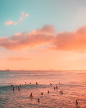 Surfers enjoy a breathtaking sunset at the beach in Honolulu, Hawaii, with vibrant sky colors.