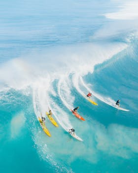 Photo by Jess Loiterton Dynamic aerial photo capturing surfers conquering massive waves in vibrant blue Hawaiian waters.