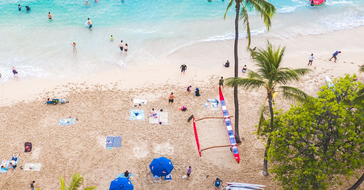 Photo by Jess Loiterton Stunning aerial shot of Waikiki Beach in Honolulu with turquoise water and palm trees.