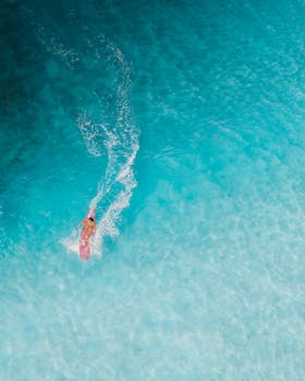 Captivating aerial shot of a surfer riding clear blue waters in Hawaii, showcasing the vibrant sea and serene surroundings.