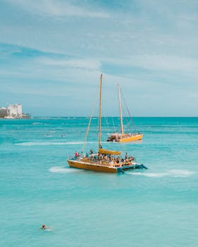 Photo by Jess Loiterton Catamarans with tourists sailing on turquoise waters under clear blue skies in Honolulu.