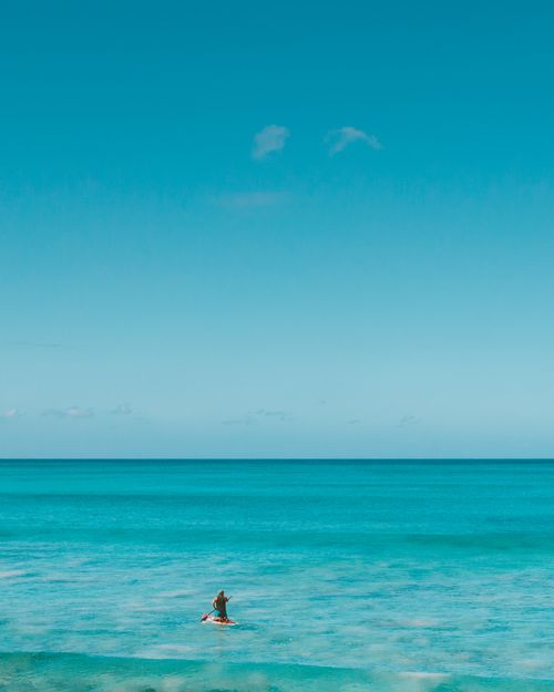Free Experience the beauty of Hawaii with a solitary paddleboarder on turquoise waters under a blue sky. Stock Photo