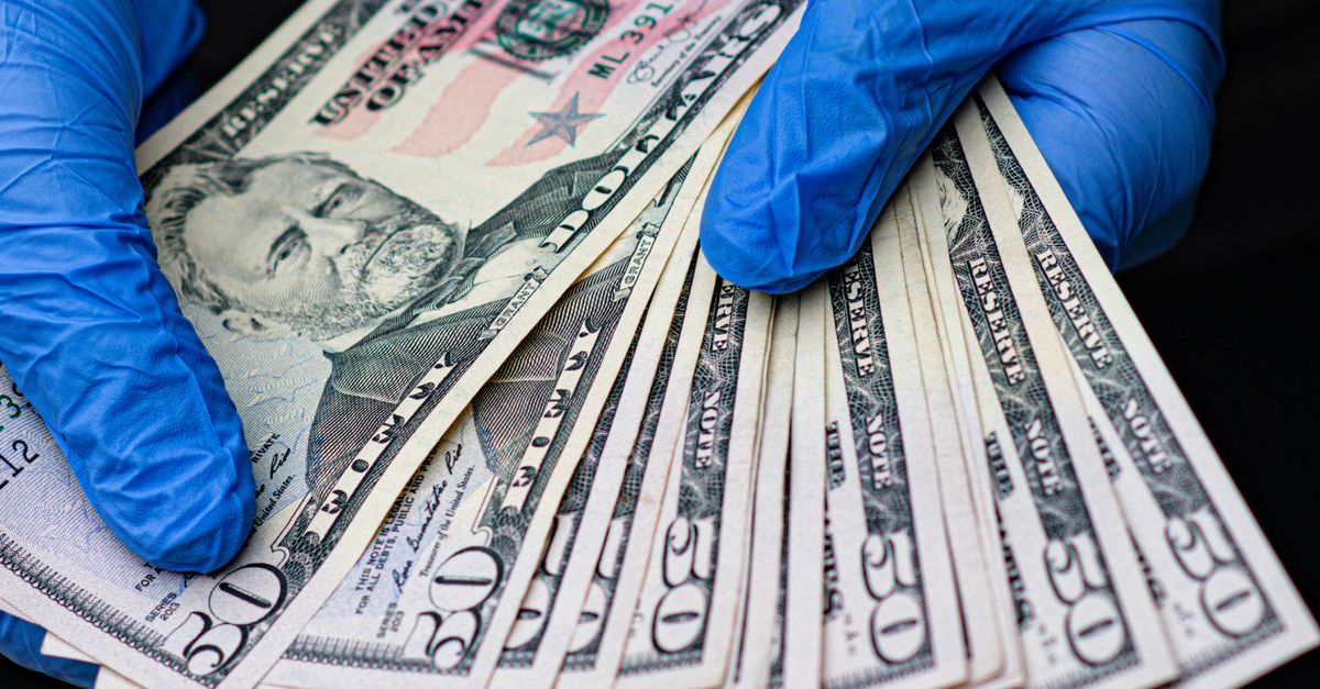 Photo by Michal Dziekonski Hands in protective gloves holding multiple US dollar bills, symbolizing virus protection and financial transactions.