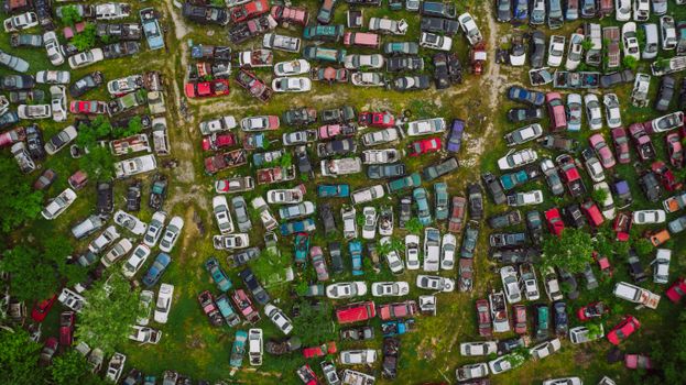 Drone top view of old desolated vehicles of different colors in automobiles graveyard