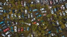 Aerial top view of numerous abandoned rusted vehicles parked in chaotic order in green automobile graveyard in suburban district