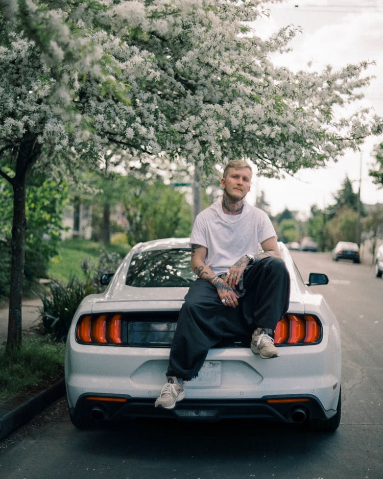 Tattooed Man Sitting On Trunk Of Luxury Car On Street