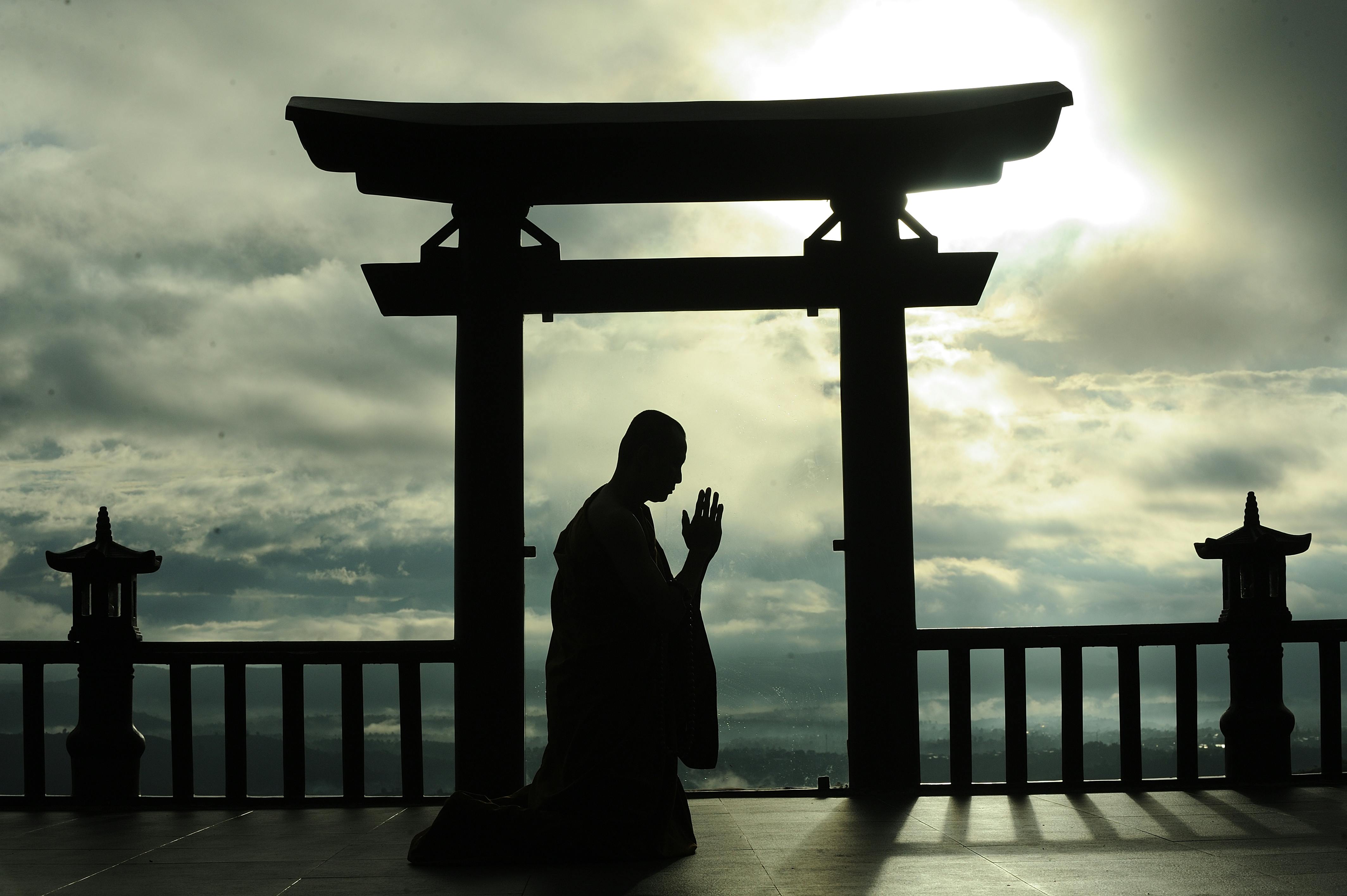 Silhouette of a man meditating in prayer under a Torii gate at sunrise, symbolizing peace and spirituality.