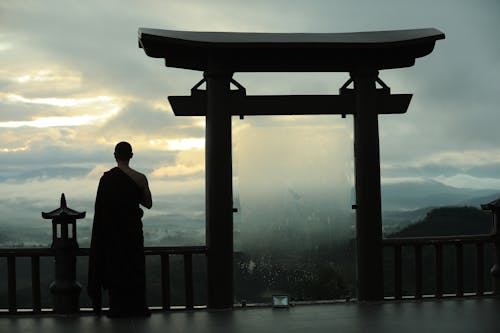 Unrecognizable monk standing near sacred Torii Gates of Buddhist sanctuary