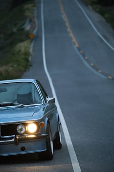 Classic vintage car on an empty road at twilight with headlights on