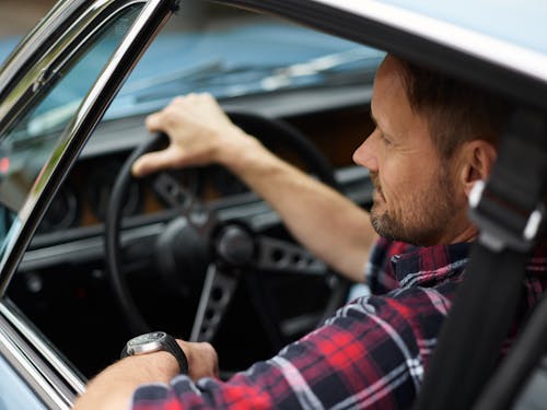 Free From above back view of confident male with short beard and mustache in plaid shirt sitting in automobile with hand on steering wheel Stock Photo
