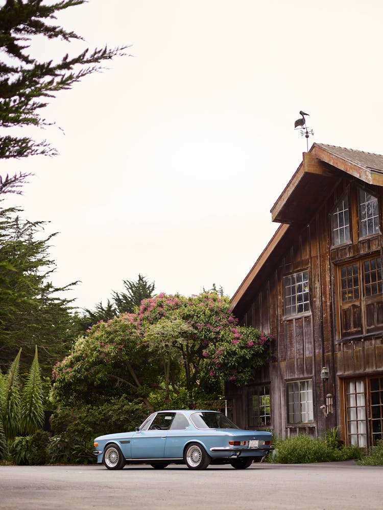 Retro Car Parked Near Old Wooden House And Green Trees