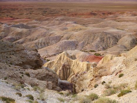 Scenery view of dry shabby rocky formations with grass on surface surrounded by dunes in desert in afternoon