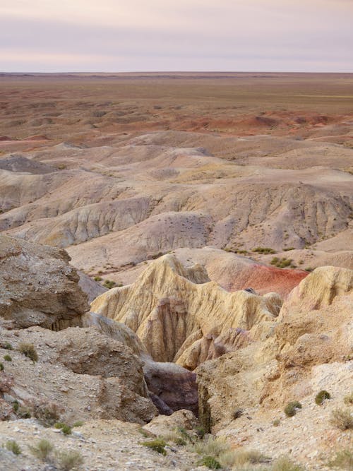 Magnificent view of rocky hills with bunches of grass surrounded by barren terrain on horizon under cloudy sky in afternoon