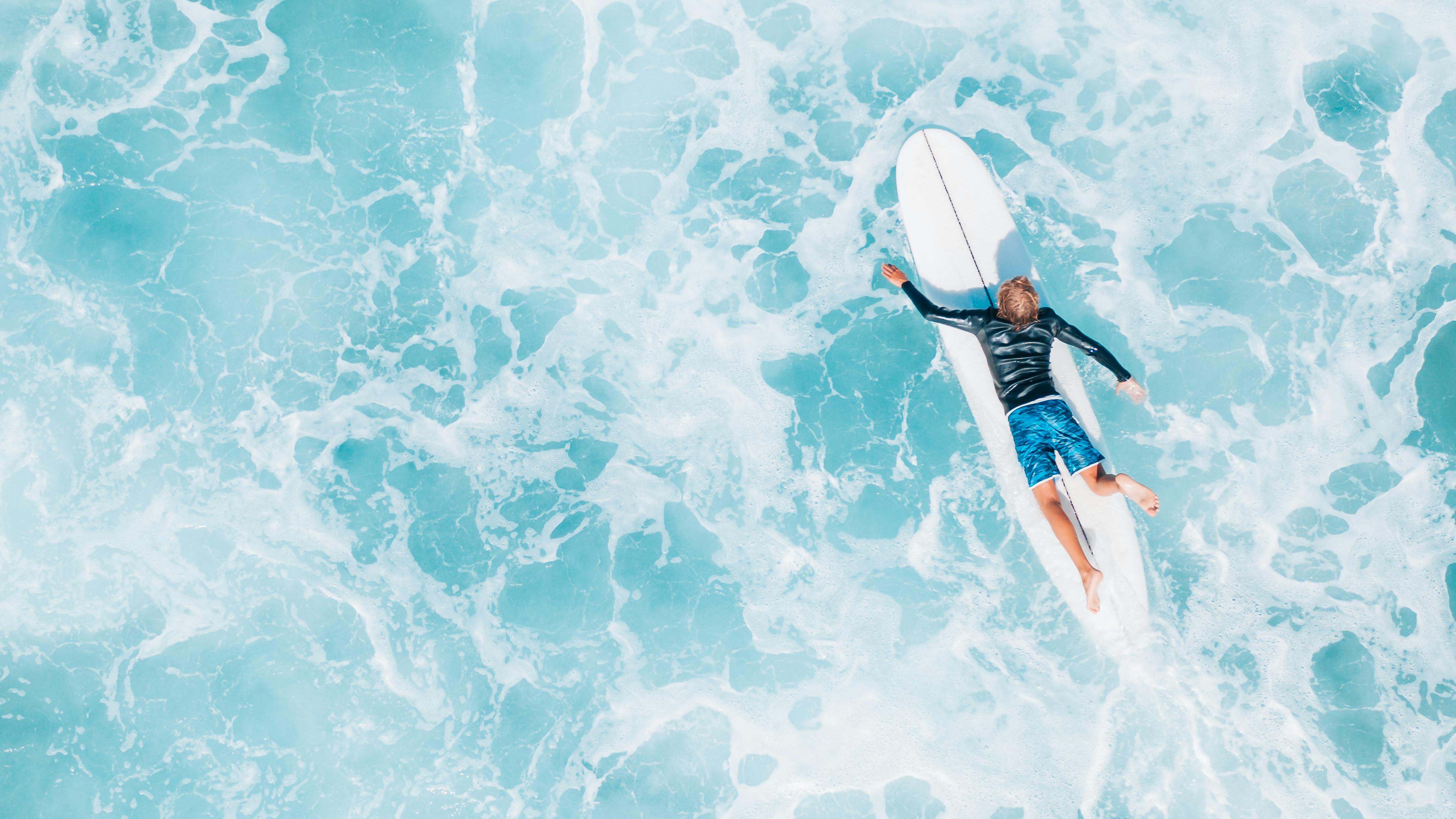 woman in black and red shorts and black shirt lying on white surfboard on water