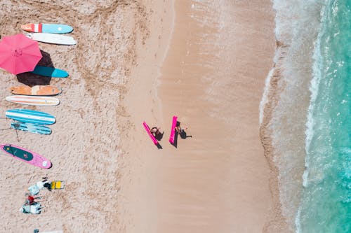 Person in Black Shirt and Blue Pants Lying on Blue Surfboard on Beach