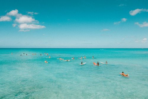 Free Aerial view of surfers waiting for waves in a clear, calm ocean under a bright blue sky. Stock Photo
