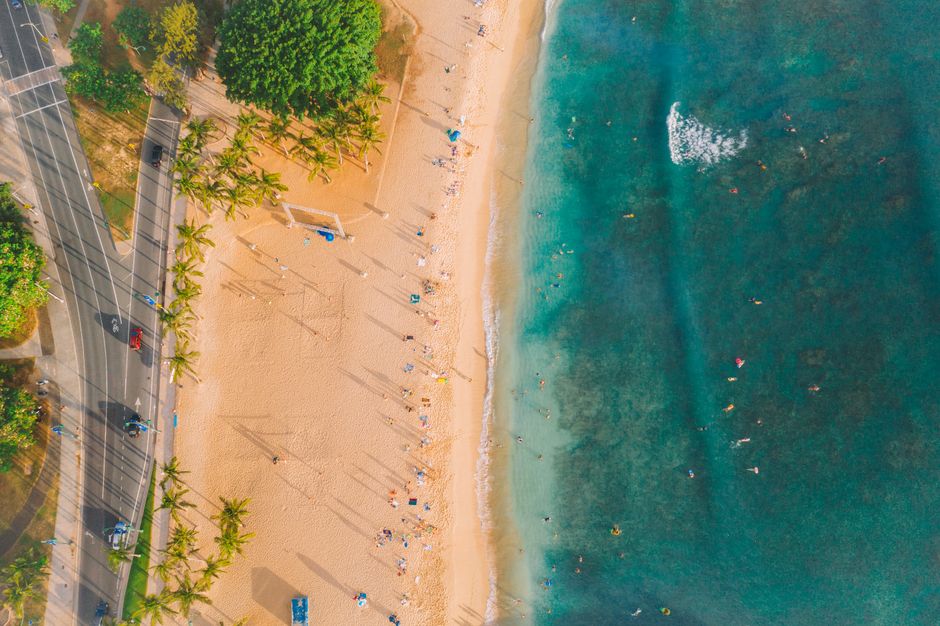 Ultimate Oʻahu Private Helicopter Experience: All Window Seats Review Review 2026 - Drone shot of Waikiki Beach, Oahu with surfers and vibrant sunset colors over the ocean.