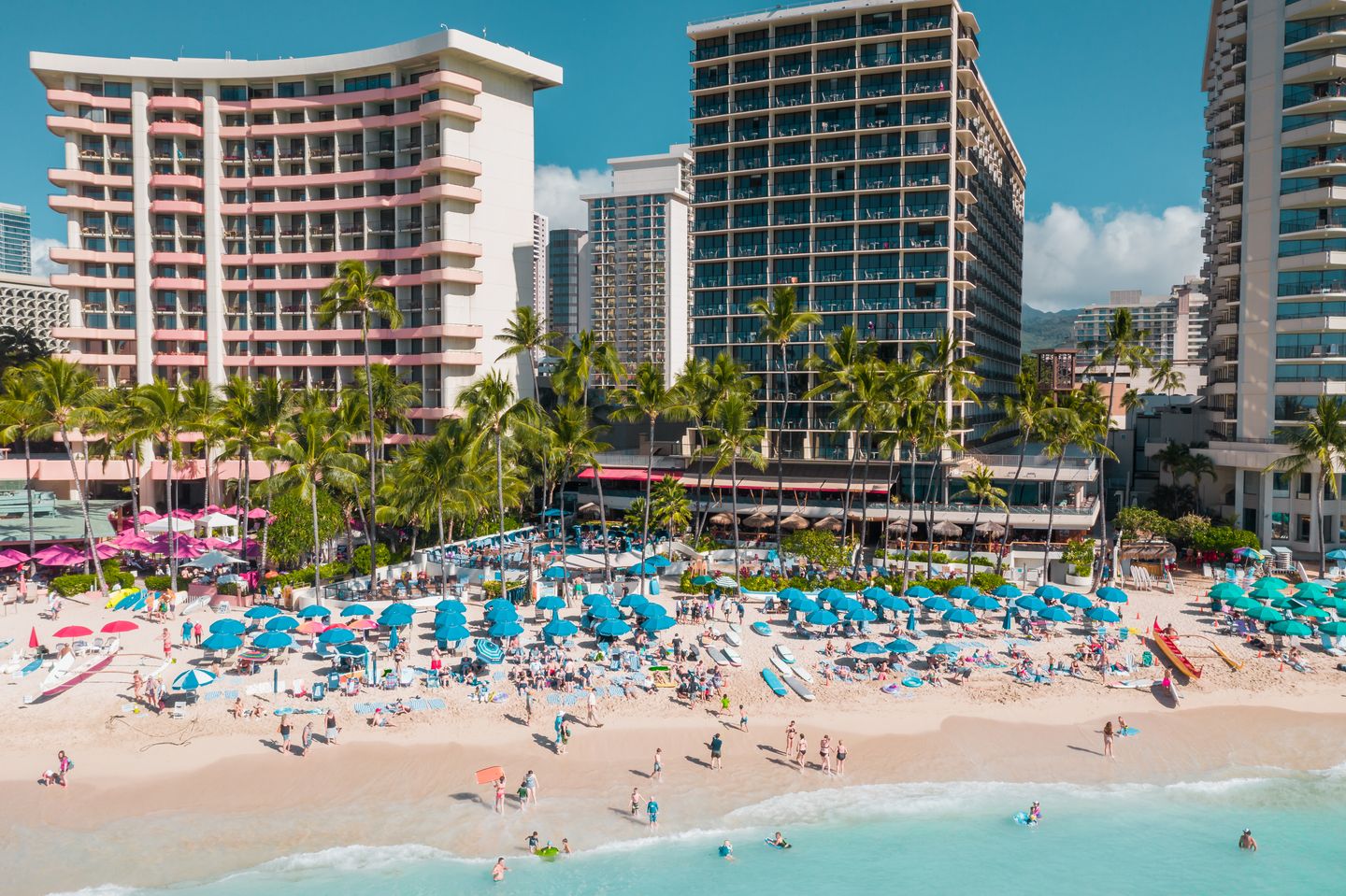 Waikīkī Beach packed with umbrellas and sunbathers, seen from above at the height of summer