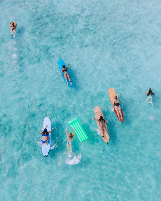 Aerial shot of surfers and swimmers enjoying crystal clear waters in Hawaii, capturing island life.