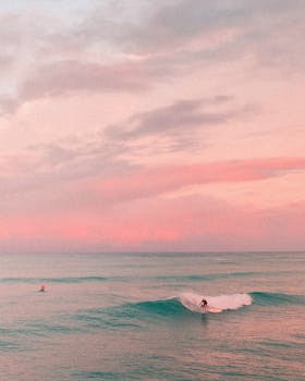 Captivating sunset scene of surfers in Honolulu, Hawaii, with pink skies and gentle waves.