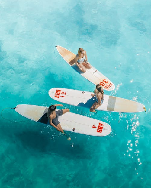 2 Men and 2 Women Riding White and Red Surfboard on Body of Water