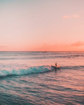 A lone surfer rides the waves during a vibrant sunset in Hawaii, capturing island paradise vibes.