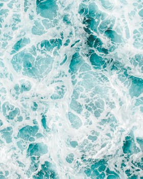 Aerial view of vibrant ocean waves and frothy seafoam creating abstract patterns.