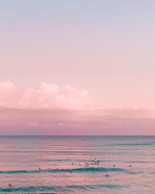 A tranquil beach sunset in Hawaii, capturing surfers enjoying the pink horizon and calm ocean waves.