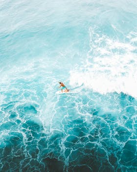 Stunning aerial shot of a surfer riding vibrant blue waves in Hawaii's ocean paradise.