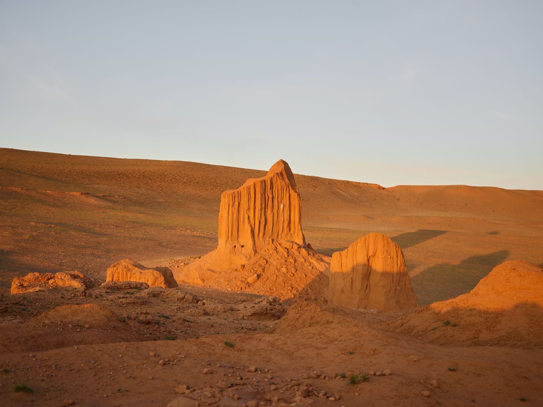 Amazing view of red sandstone cliffs in empty desert terrain under clear blue sky with long fallen shadows