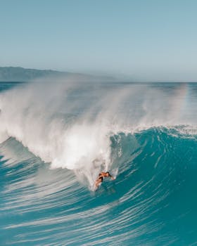 A thrilling aerial shot of a surfer riding massive waves on a sunny day in Hawaii.